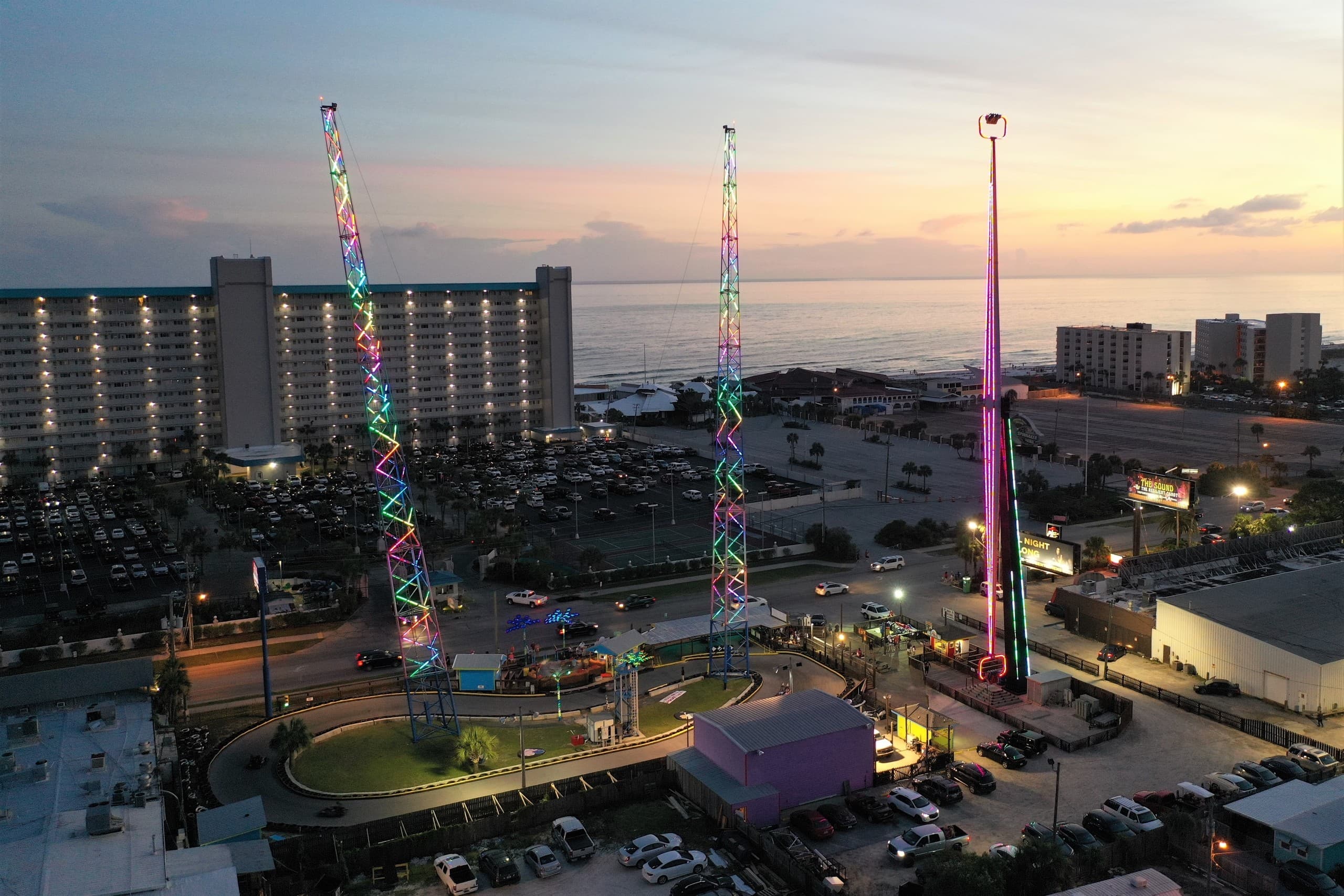 Coastal thrill ride towers lit at twilight with ocean backdrop