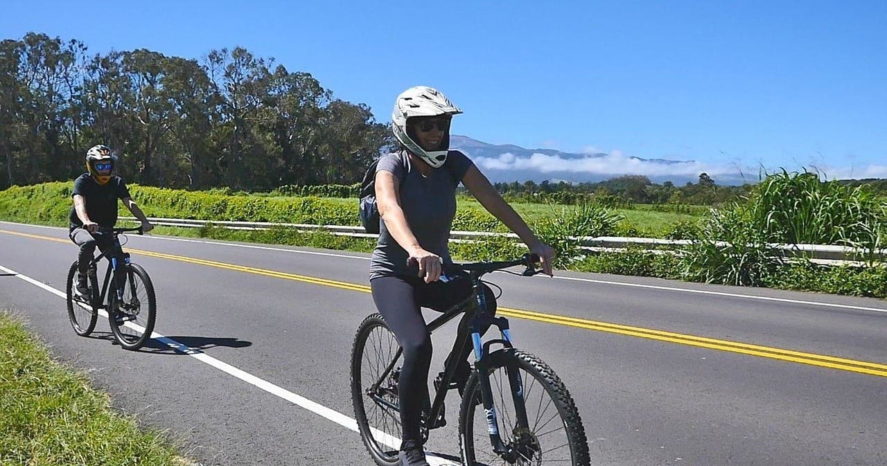Close-up cyclists on paved road through lush roadside vegetation in Maui
