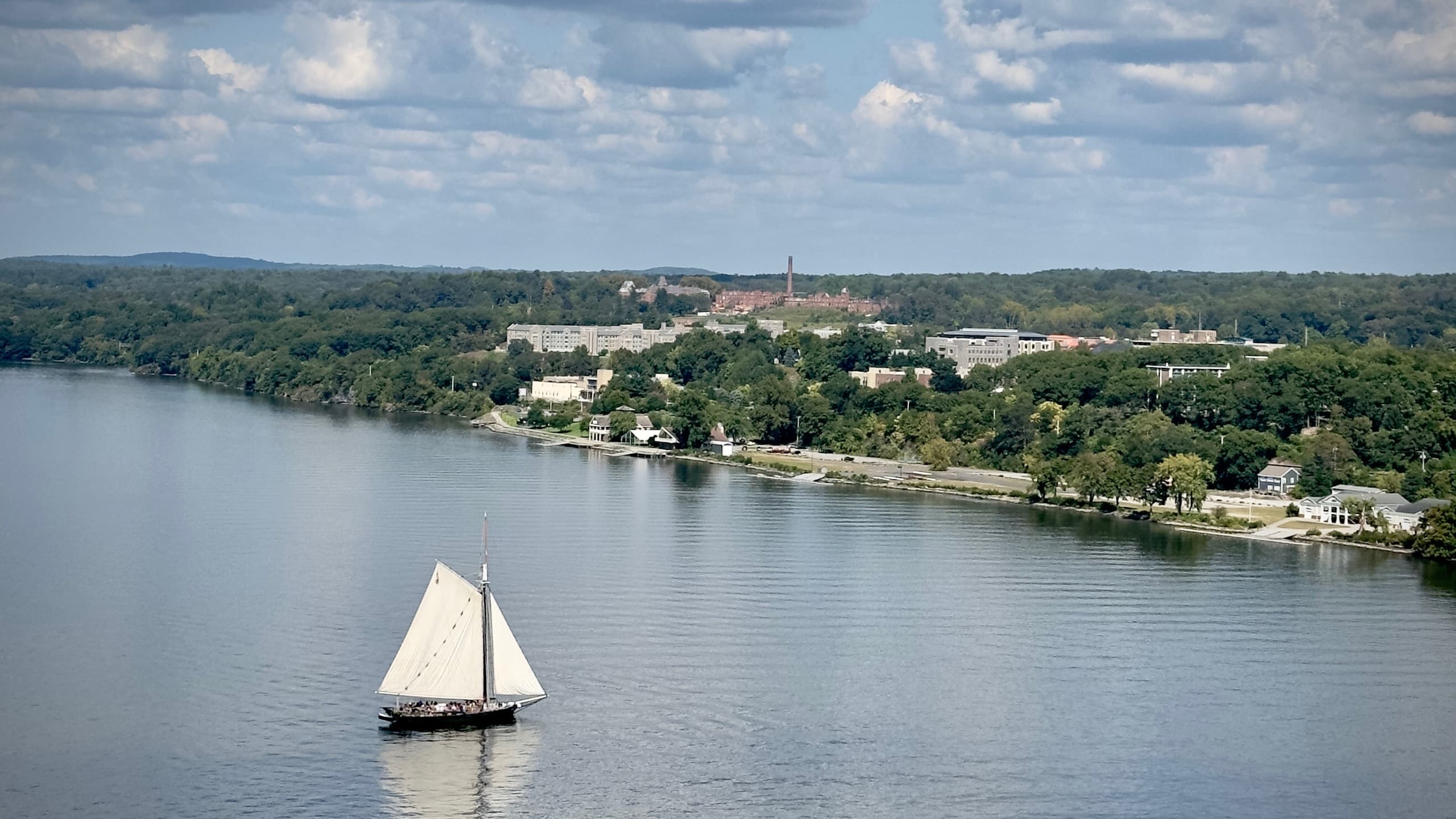Single sailboat cruising on calm river with shoreline vistas