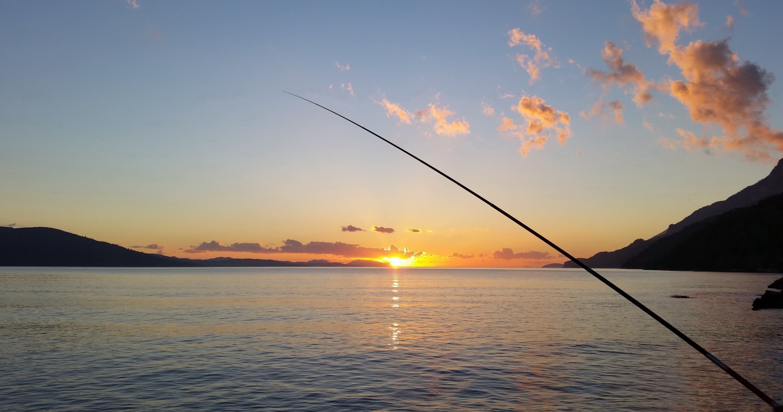 Angler fishing at sunset over calm ocean bay, scenic horizon