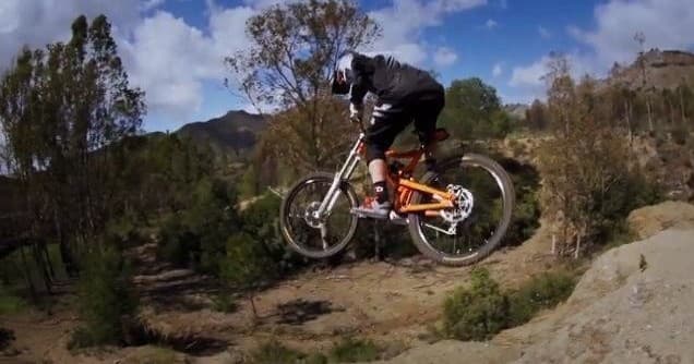Mountain biker jumping off dirt trail in rugged hillside landscape
