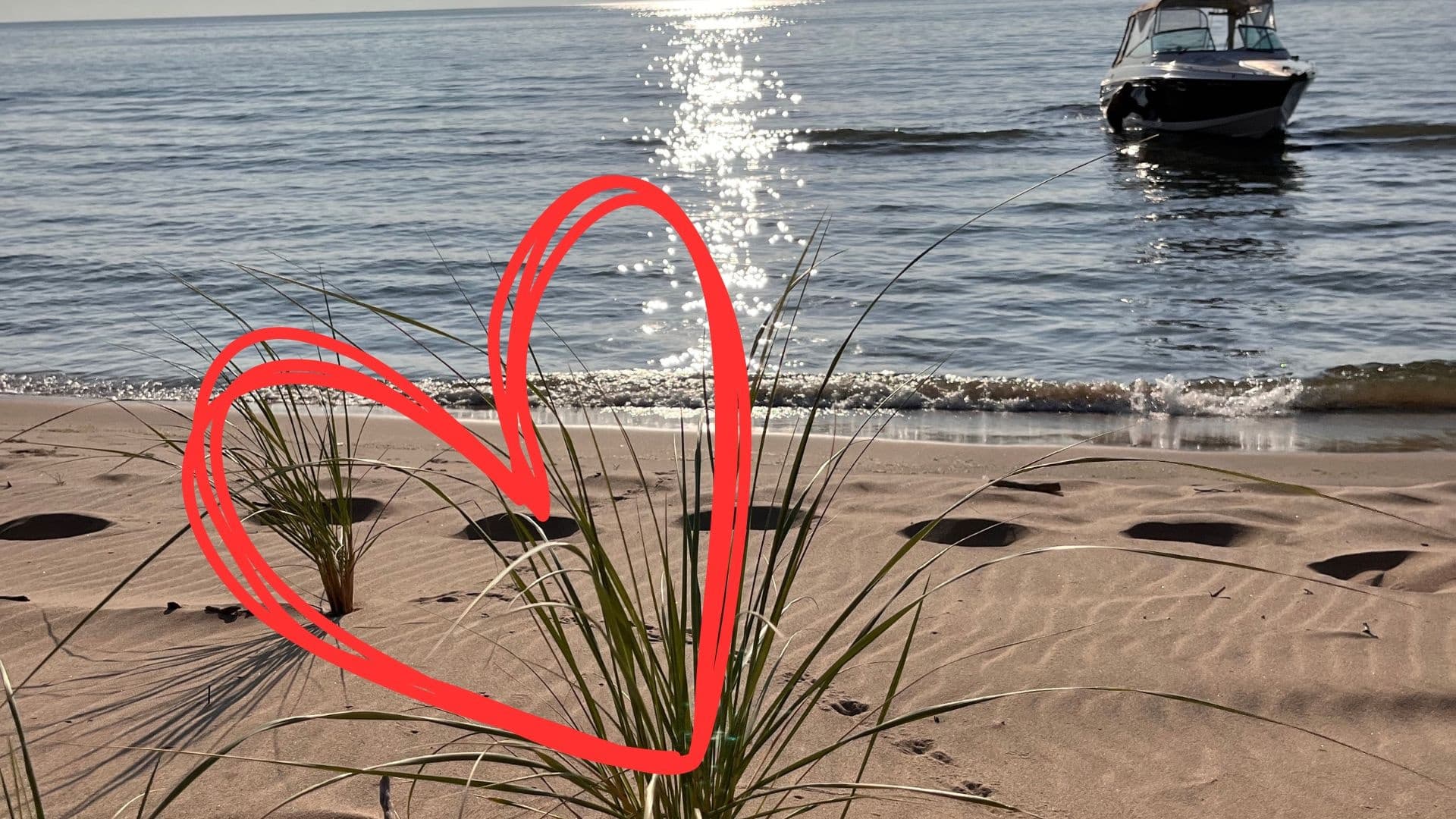 Heart drawn on sandy beach dunes with boat offshore at sunset