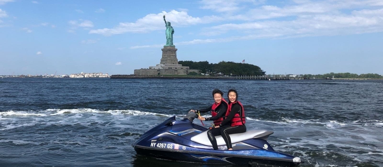 Two riders on jet ski with Statue of Liberty in background
