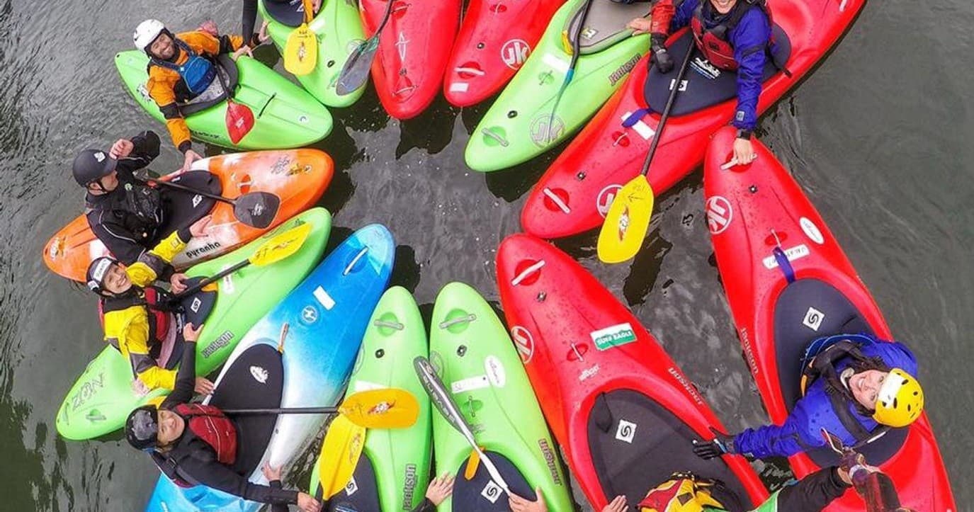 Aerial view of colorful kayaks clustered on calm river, paddlers prepping