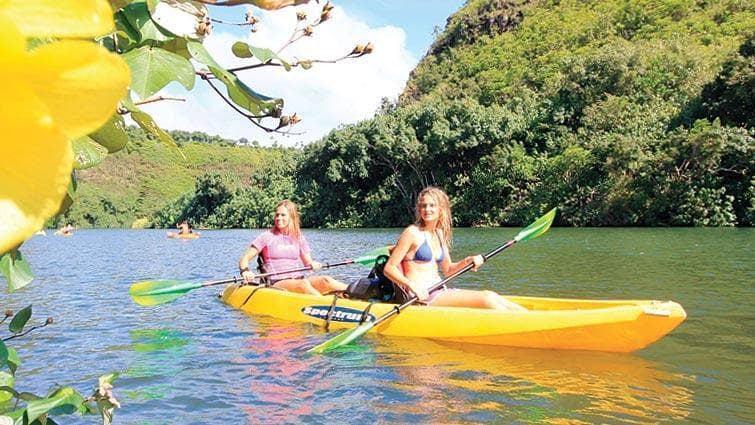 Two kayakers paddling a yellow tandem kayak on tropical river