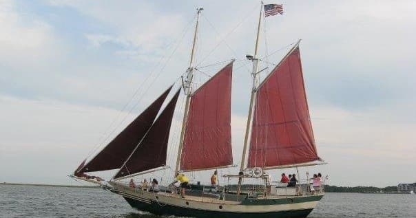 Red-sailed schooner cruising coastal waters under cloudy sky