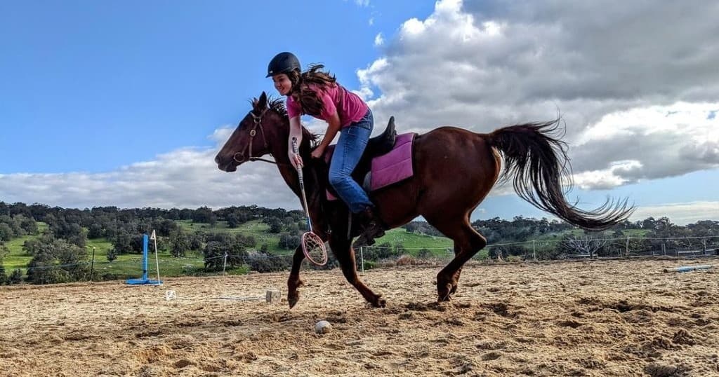 Mounted rider galloping across outdoor arena in training jump