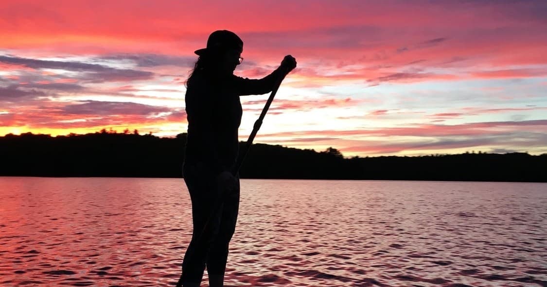 Stand-up paddler silhouetted at sunset on a calm lake