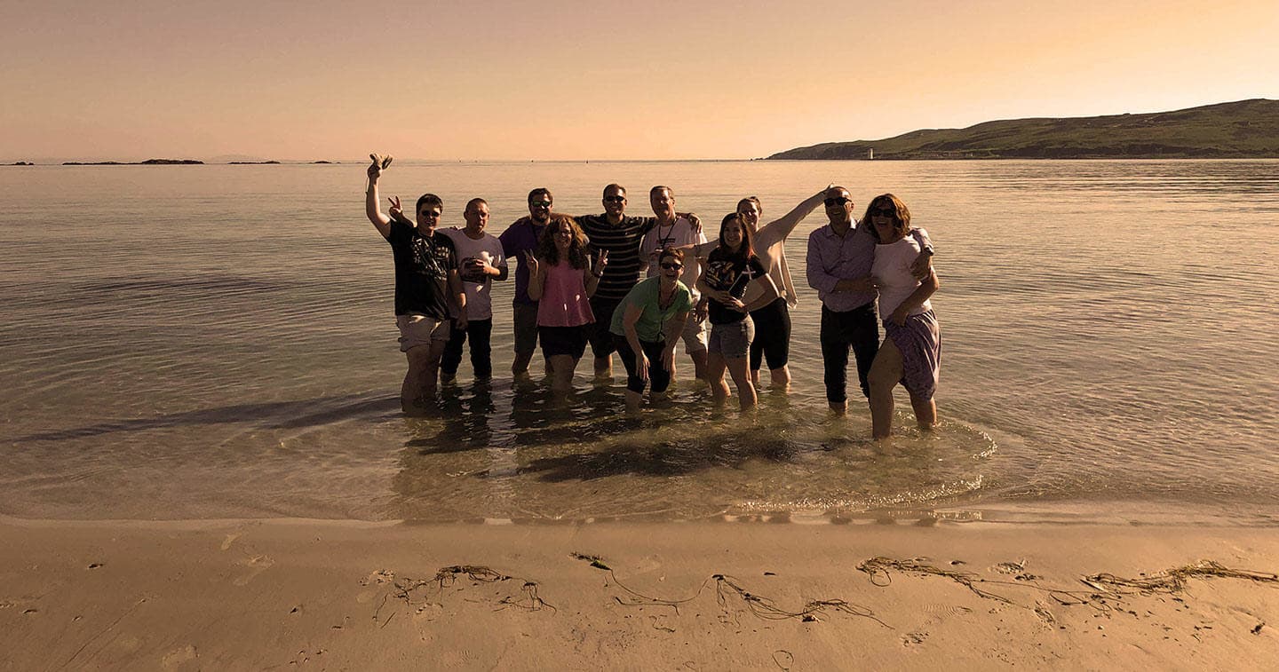 Friends wading on a sandy Scottish beach at golden sunset