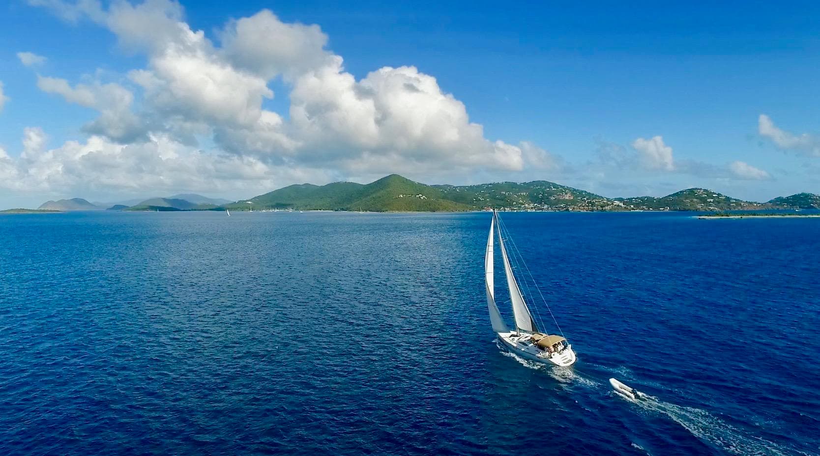 Sailboat cruising the blue Caribbean Sea toward island horizon