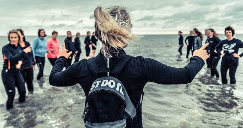 Leader guiding wetsuit group running through surf on coastal beach