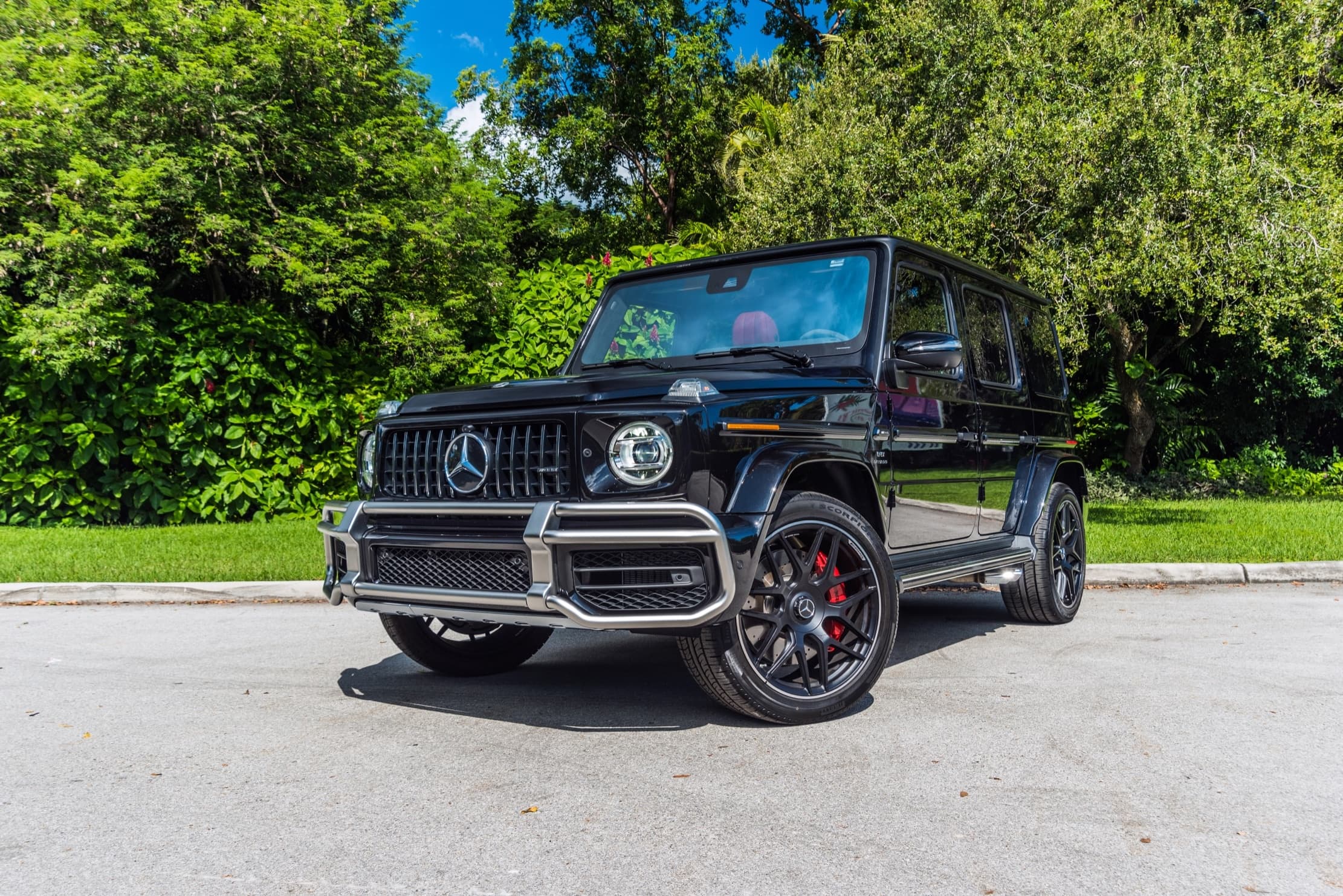 Black Mercedes G-Wagon parked by green foliage on sunny drive
