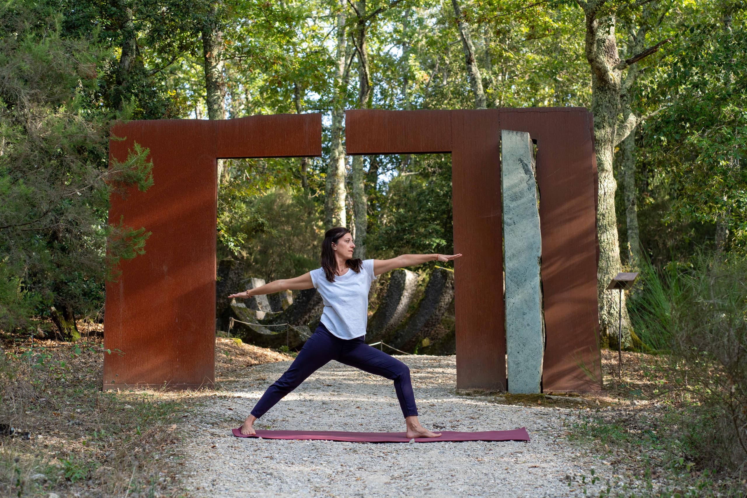 Person practicing yoga by rusted sculptures on wooded Chianti park trail