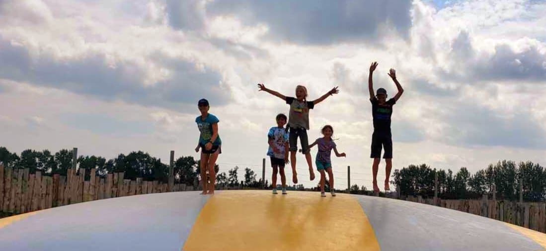 Kids jumping on inflatable farm pillow under cloudy sky