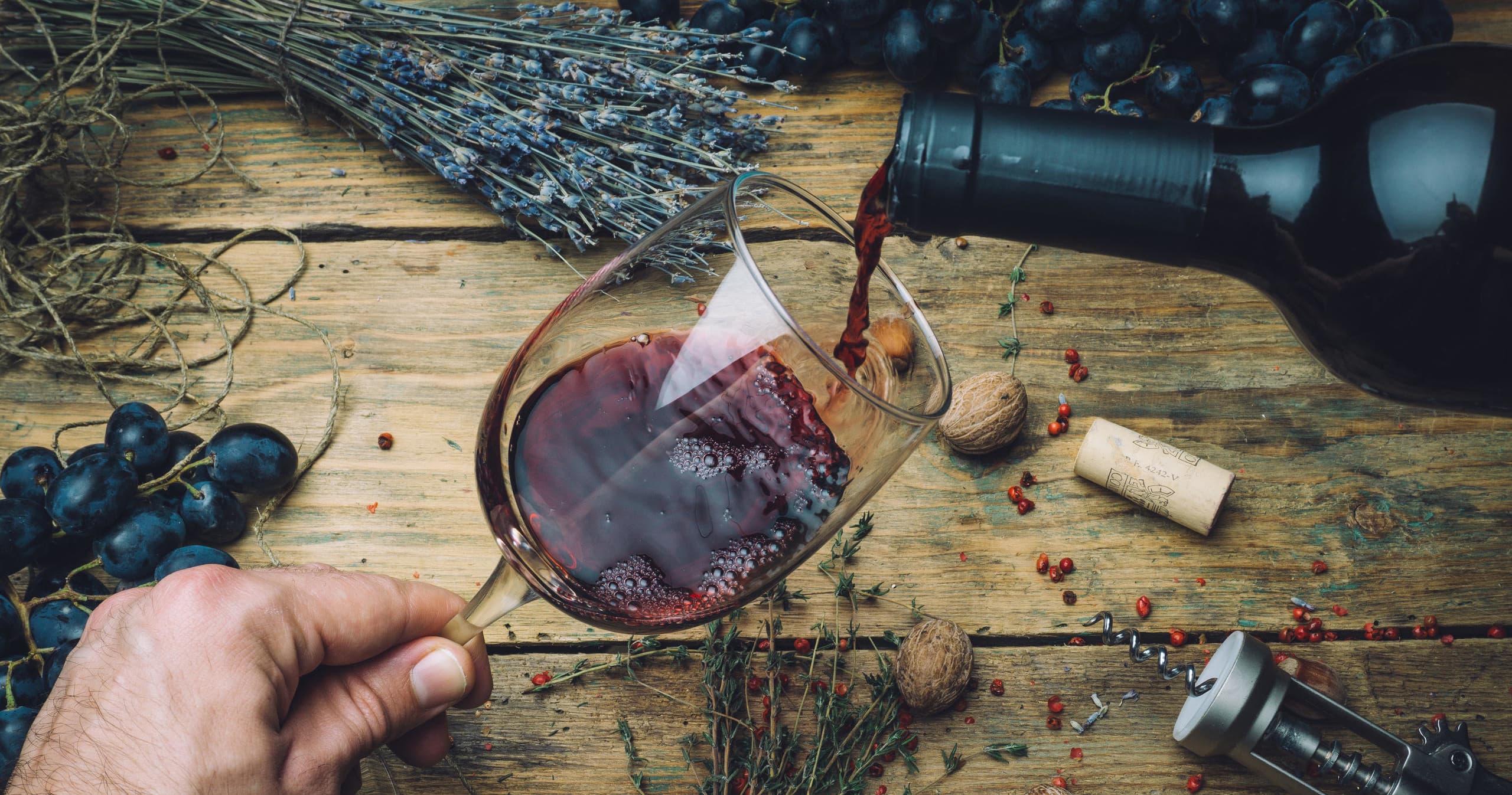 Pouring red wine over rustic table with grapes outdoors