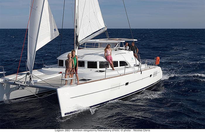 White catamaran cruising blue open sea with sailing crew