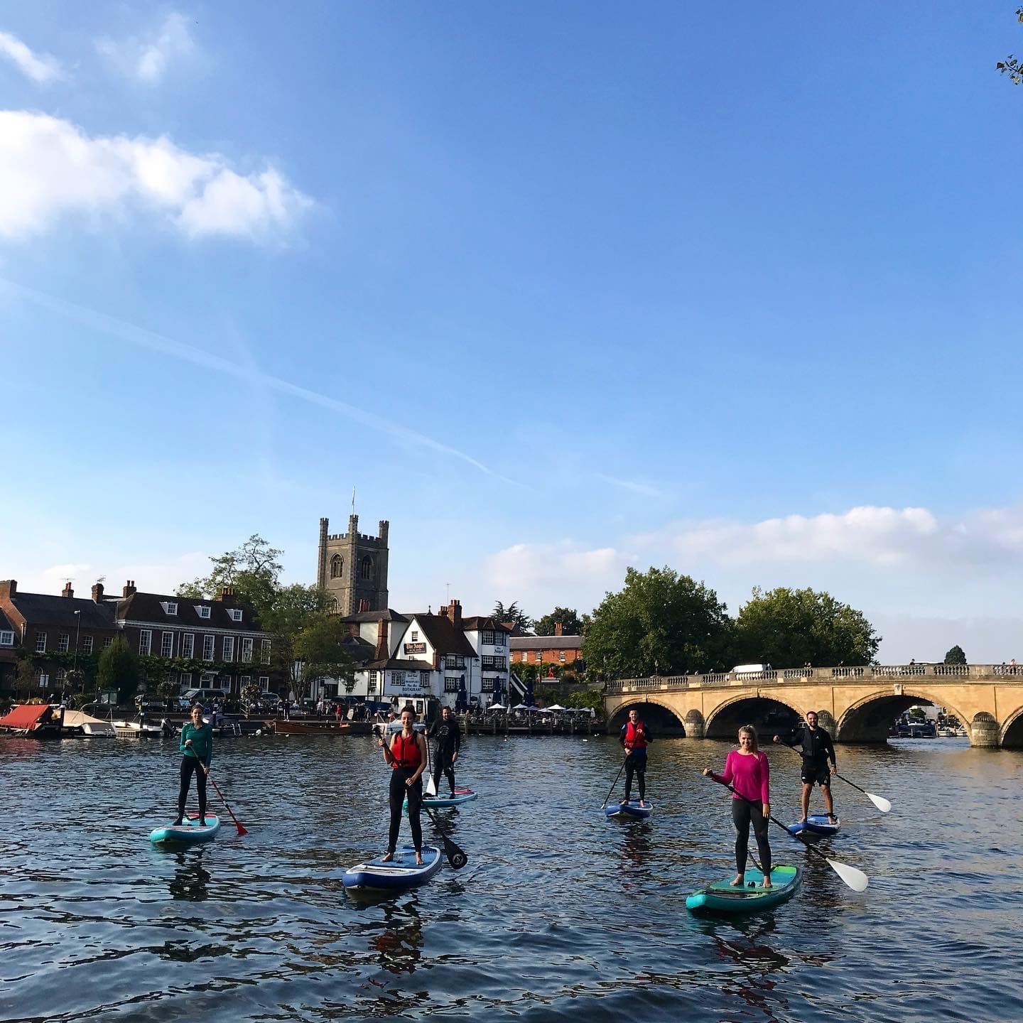Group paddleboard tour passing historic stone bridge in town