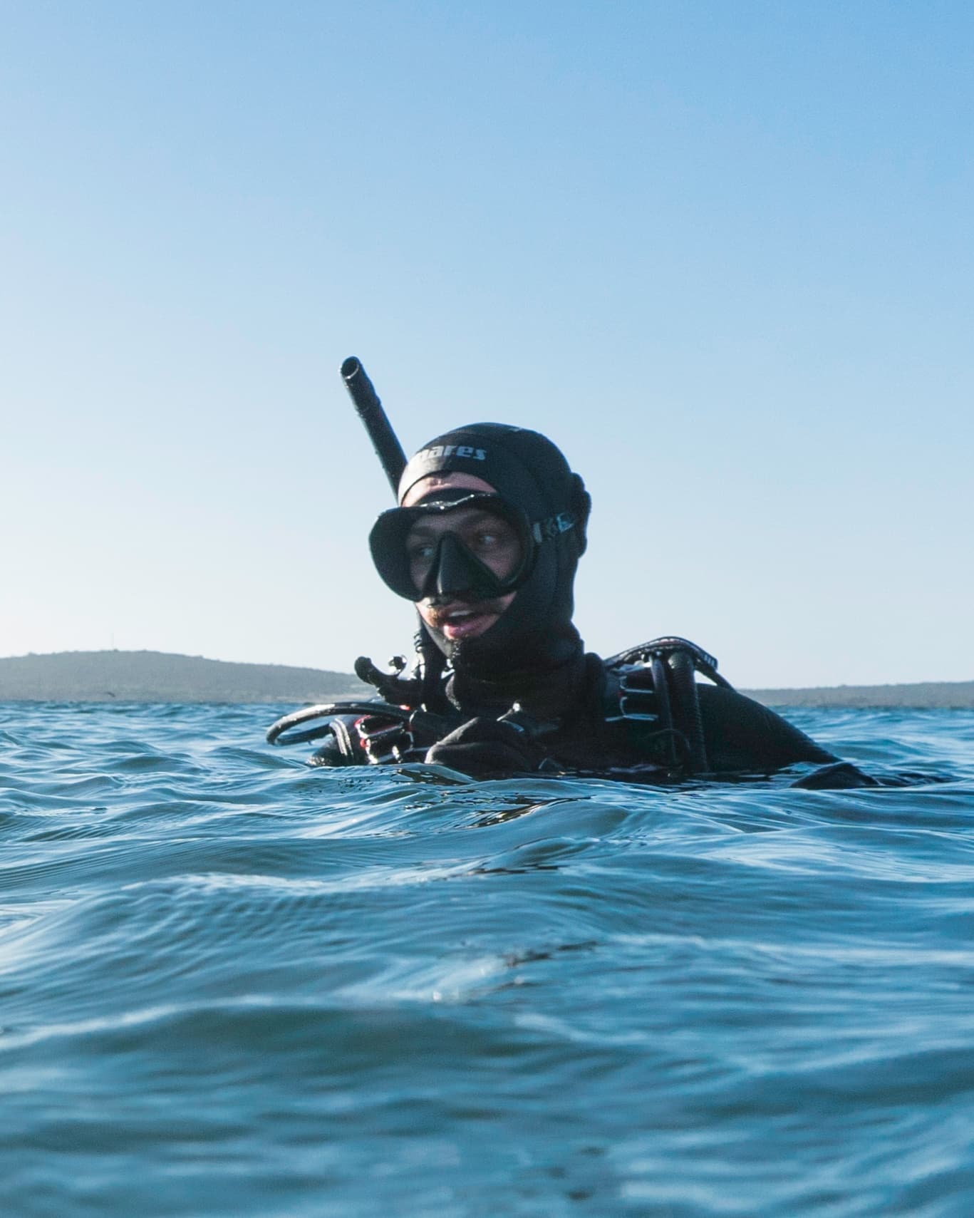 Wetsuited diver bobbing at water surface with snorkel near coast