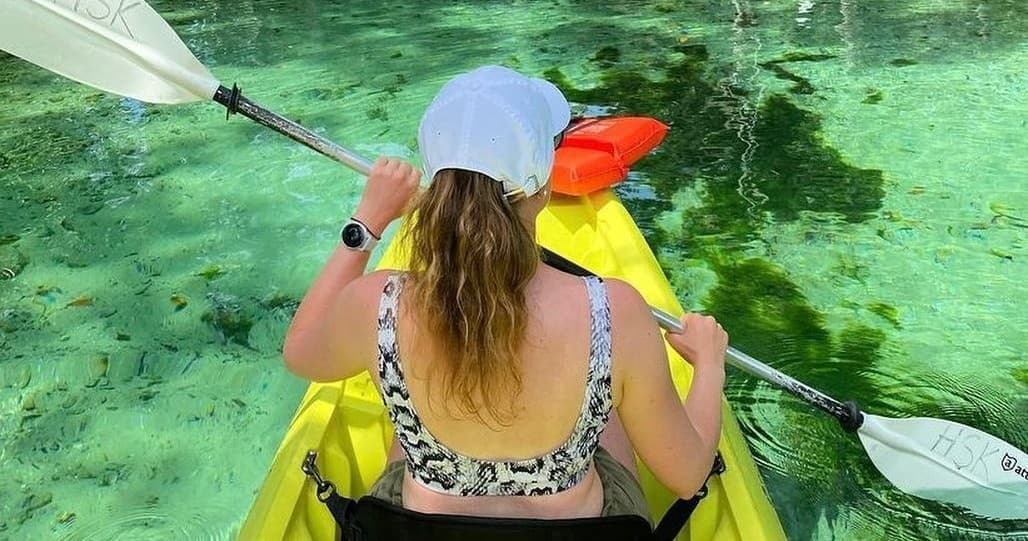 Paddler kayaking through crystal clear spring with lush shoreline