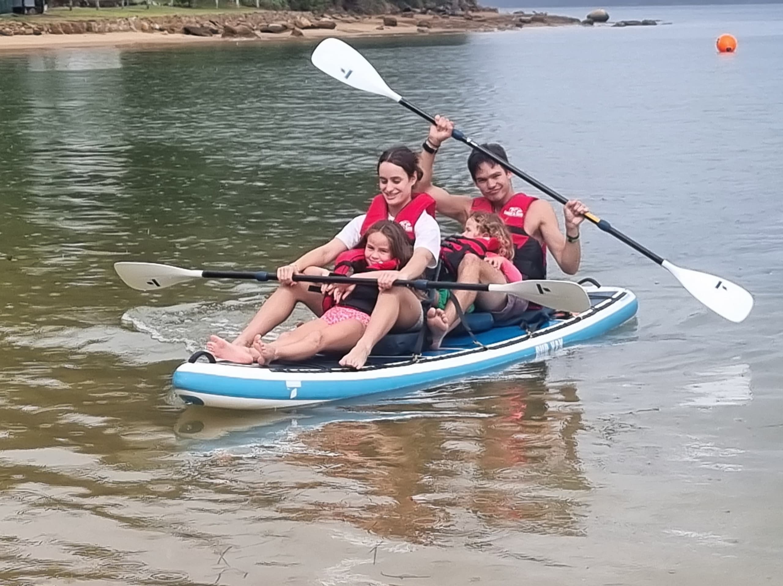 Family paddling inflatable kayak near shallow coastal bay