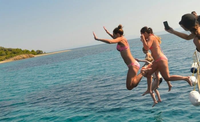 Group jumping off yacht into clear coastal sea for summer swim