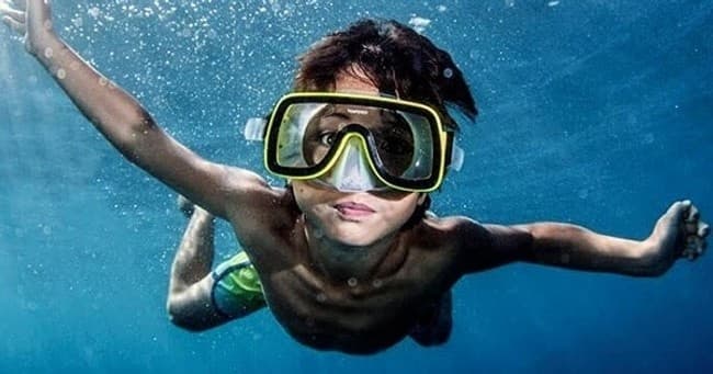 Child snorkeling underwater with mask and fins in tropical ocean