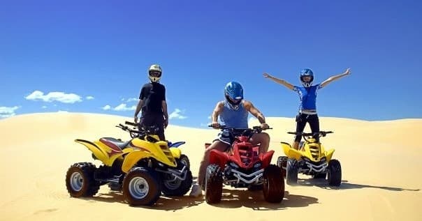 Group of three ATVs and riders posing on sunny Pismo dunes