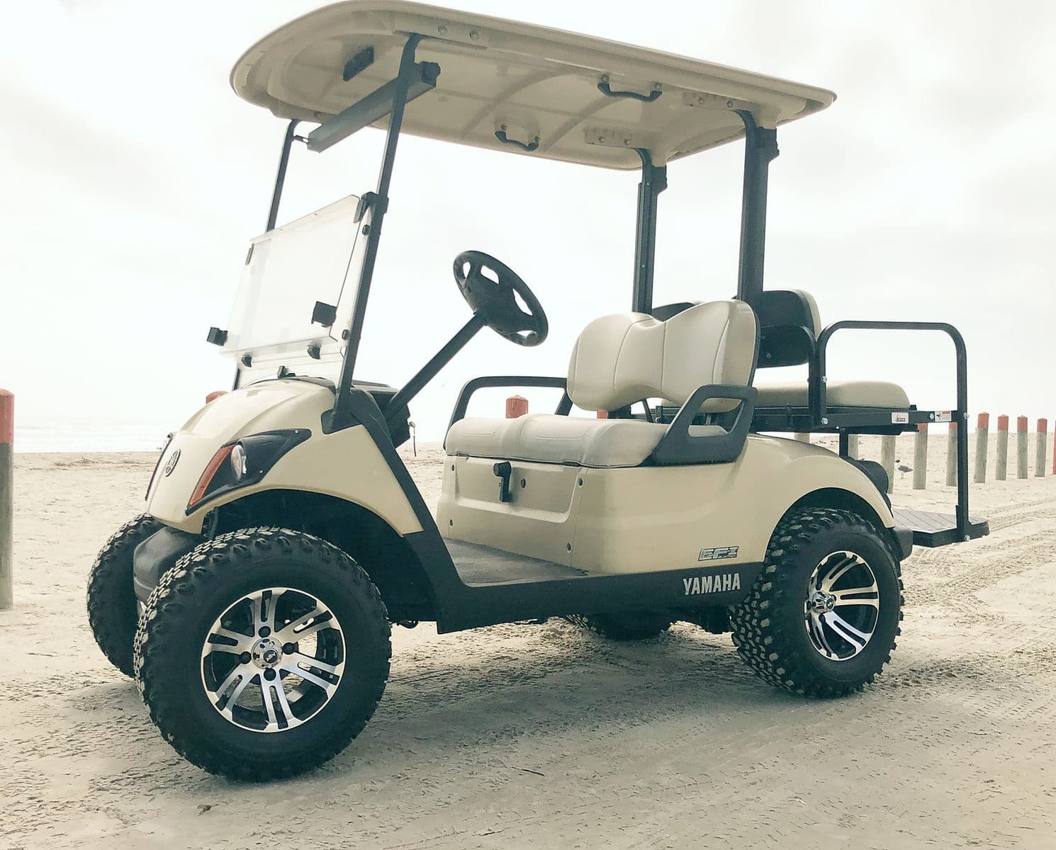 Beige beach golf cart with lifted tires on coastal sand