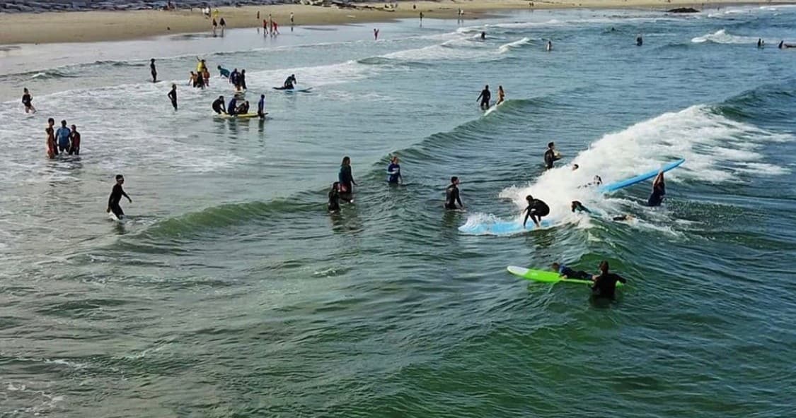 Crowded surf lineup with many surfers catching small waves