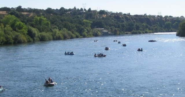 Rafting groups on wide scenic river through tree-lined valley