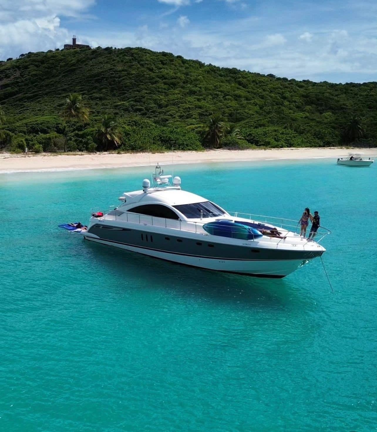 Yacht anchored in shallow turquoise bay with green hillside