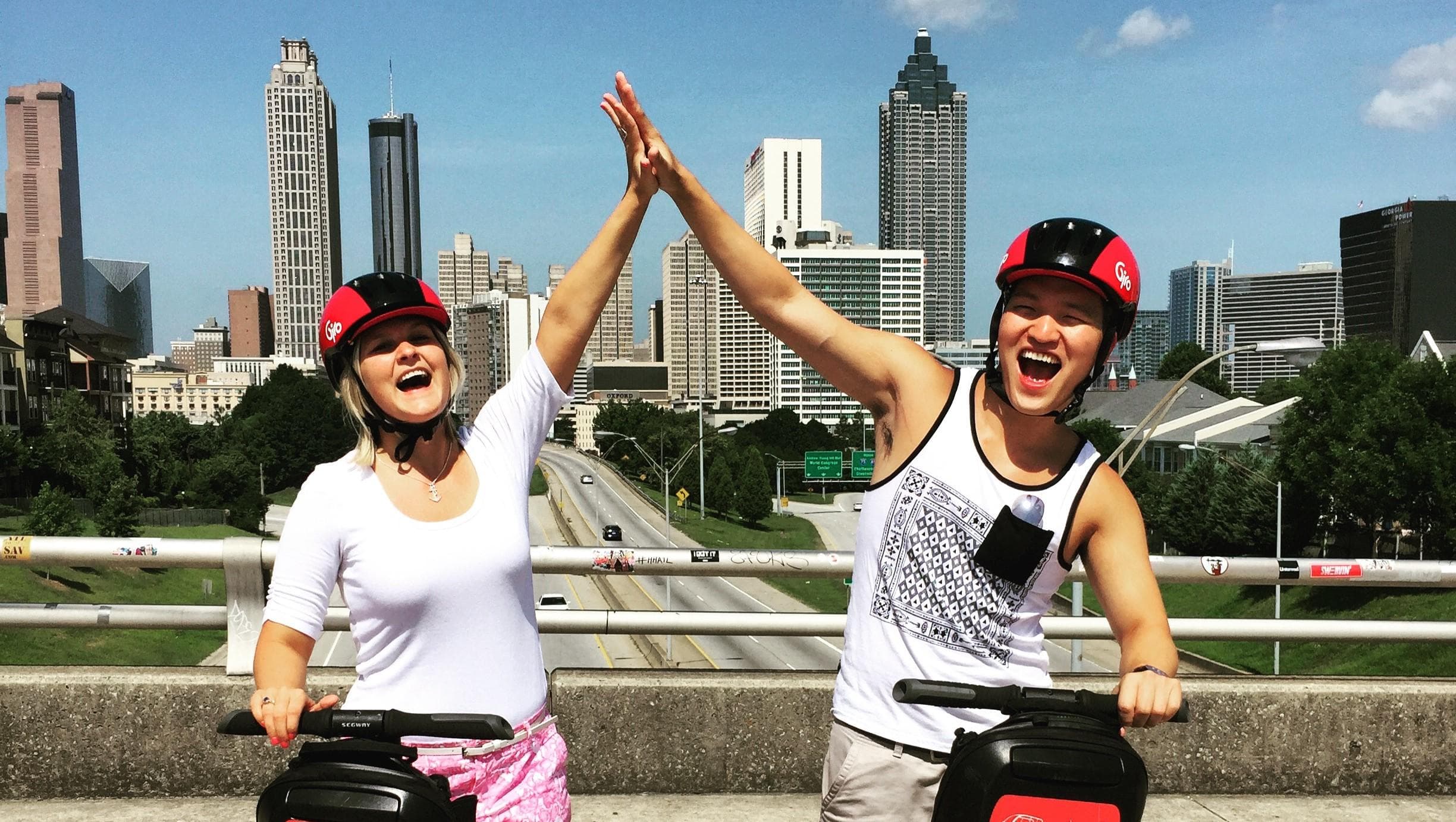 Two riders high-fiving on Segways with Atlanta skyline backdrop