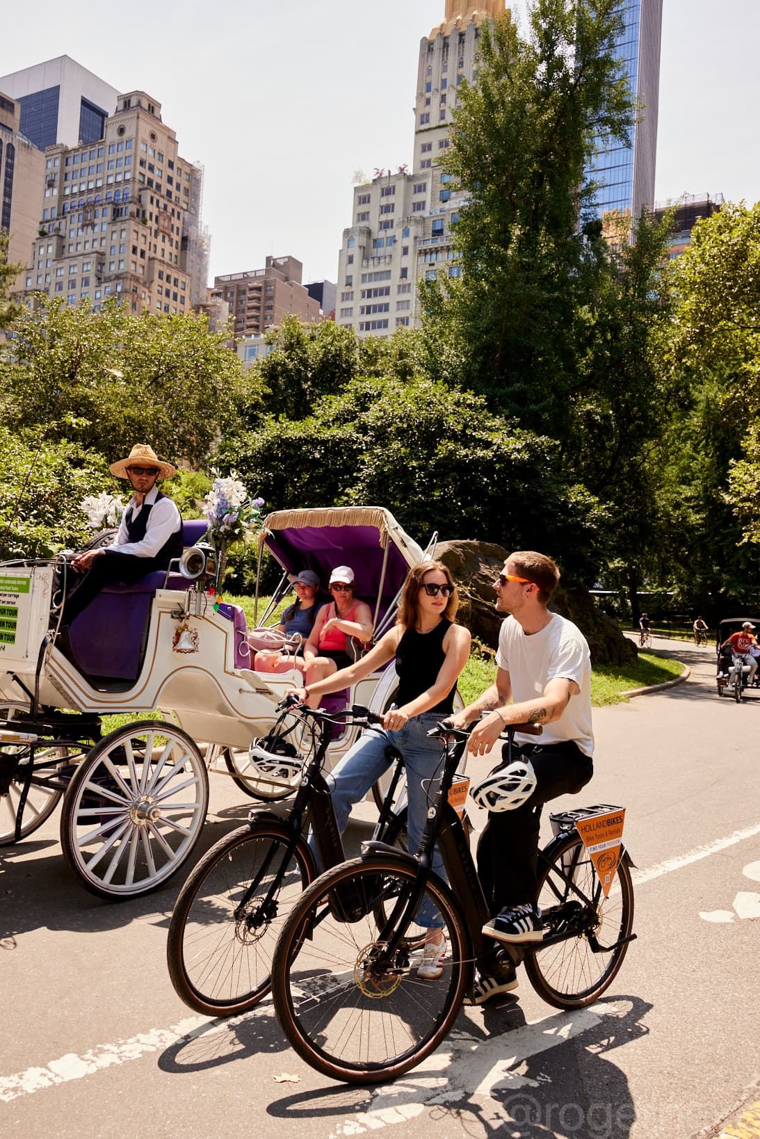 Couple riding bikes in Central Park with carriage and cityscape