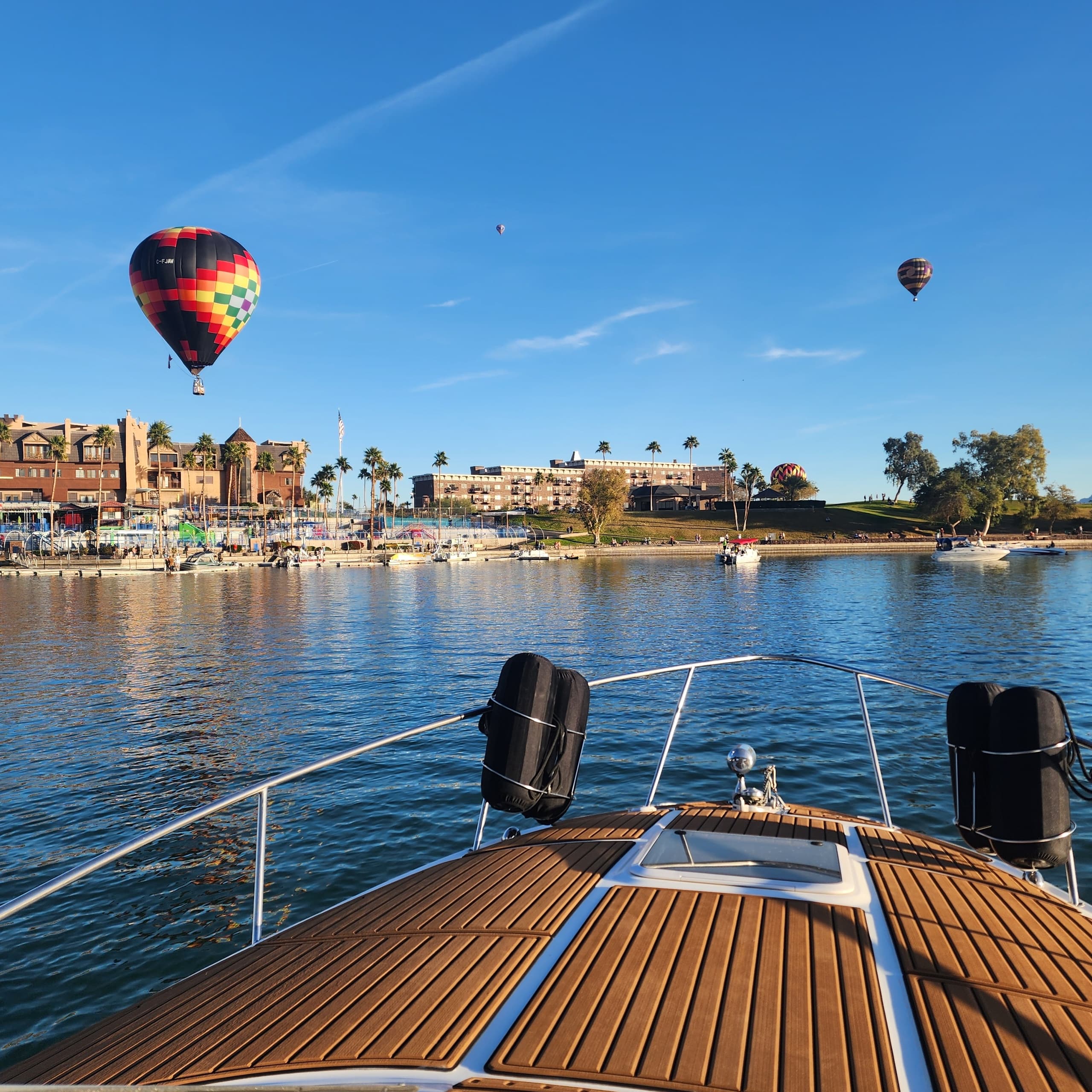 Boat bow cruising past lakeside town with hot air balloons