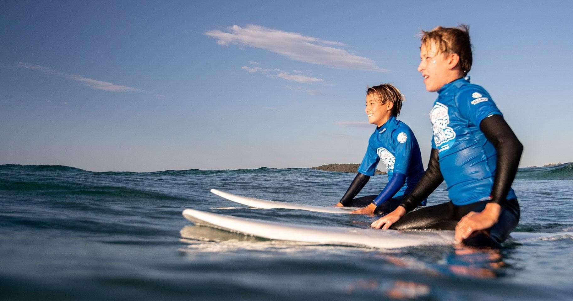 Two young surfers sitting on boards in clear sea water, peaceful surf