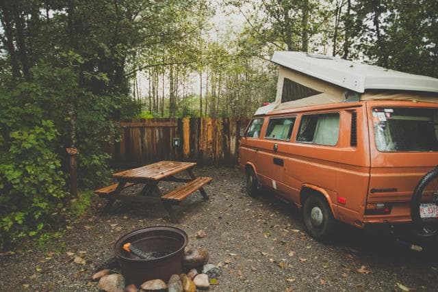 Retro camper van at forest campsite with picnic and firepit