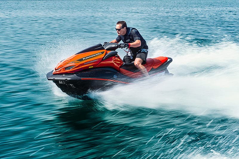 Man riding orange jet ski speeding across turquoise ocean water