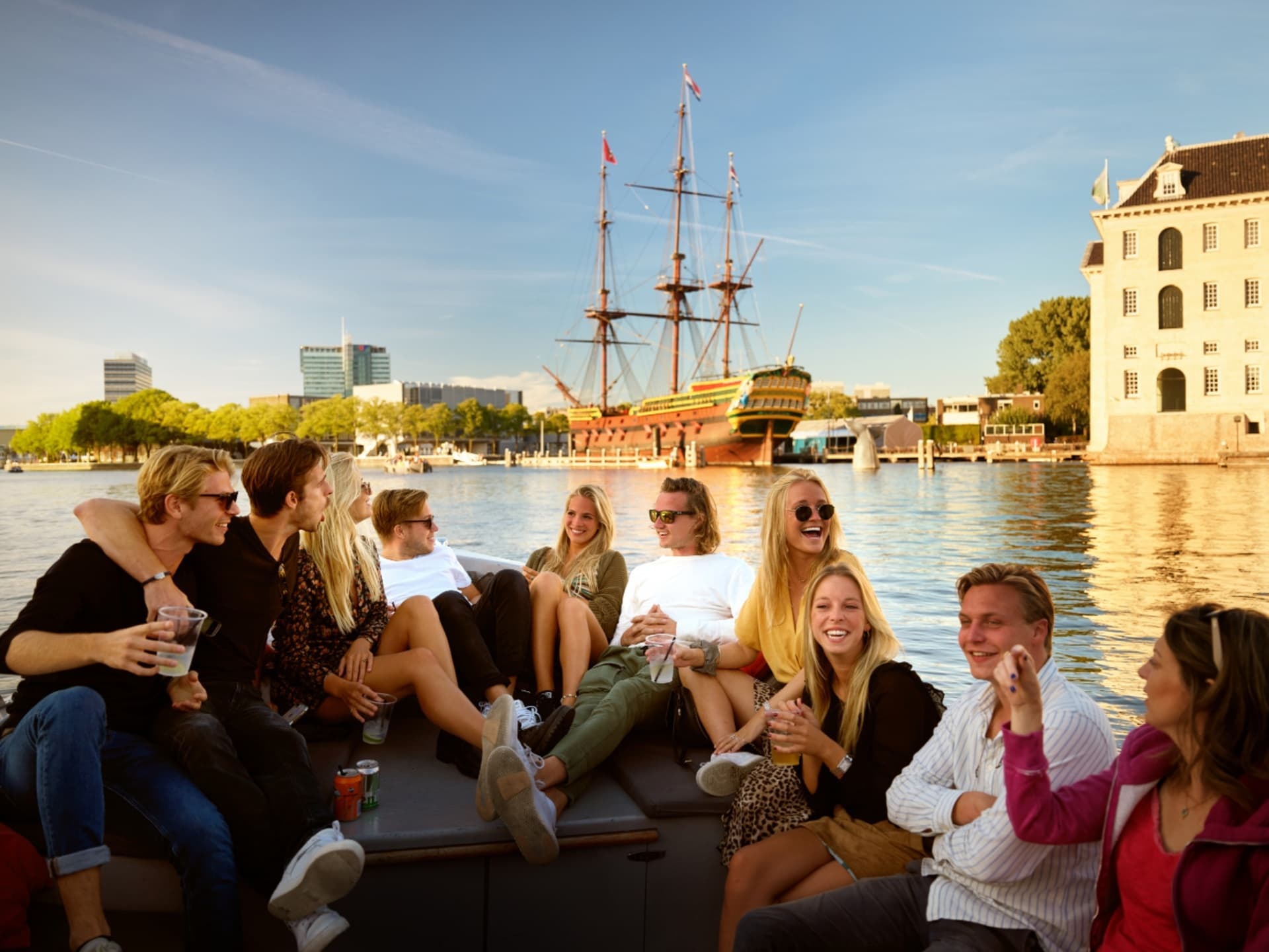 Group enjoying sunny Amsterdam canal cruise near historic ships