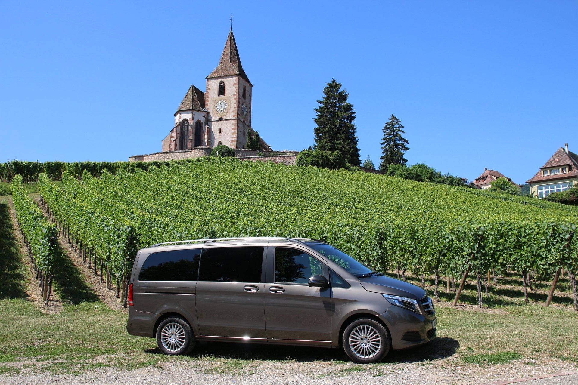 Minivan parked by scenic Alsace vineyard with hilltop church