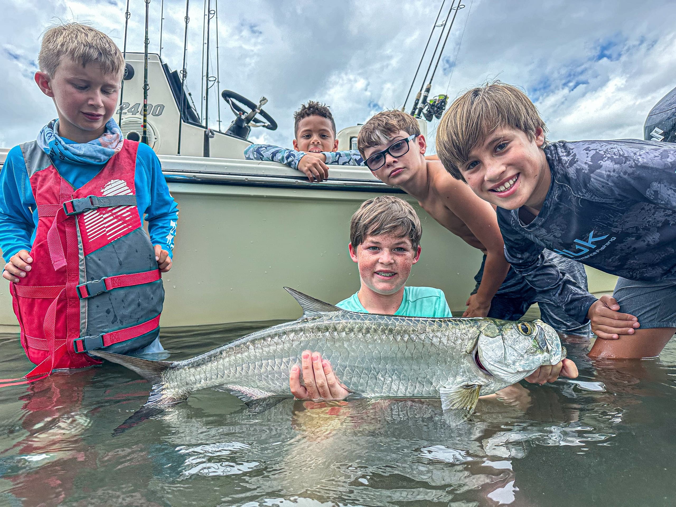Kids holding a tarpon in shallow coastal flats near boat