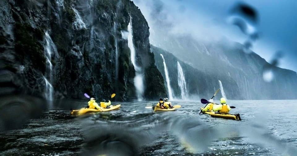 Group kayaking beneath waterfalls along Milford Sound cliffs