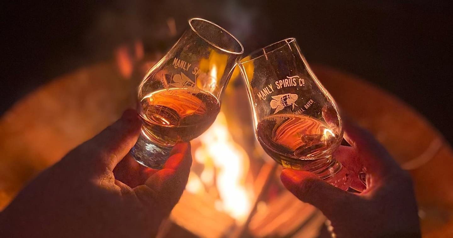 Friends toasting whiskey by outdoor firepit at a rustic campsite