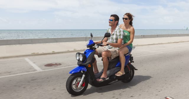 Two people riding scooter on seaside road, scenic coastal ride