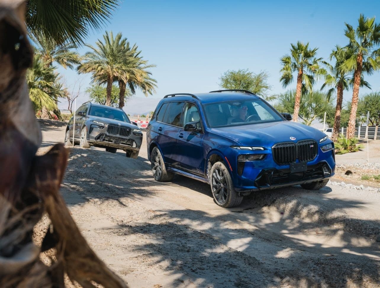 BMW SUVs off-roading through desert palm landscape, sandy trail