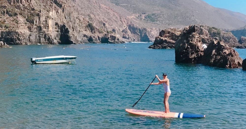 Stand-up paddleboarding near rocky coastal cove and clear water