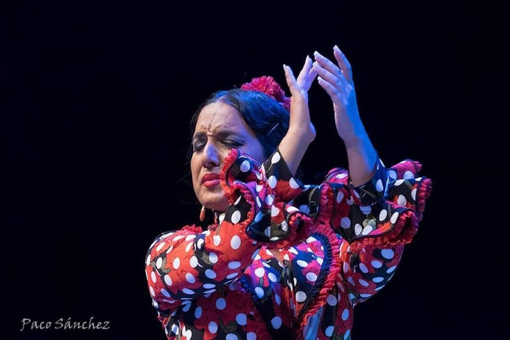 Flamenco dancer performing on dark stage in dramatic pose