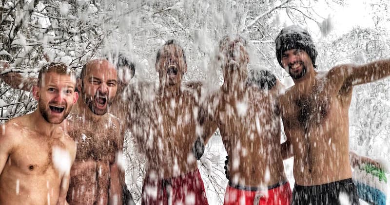 Men taking icy plunge and splashing in snowy forest