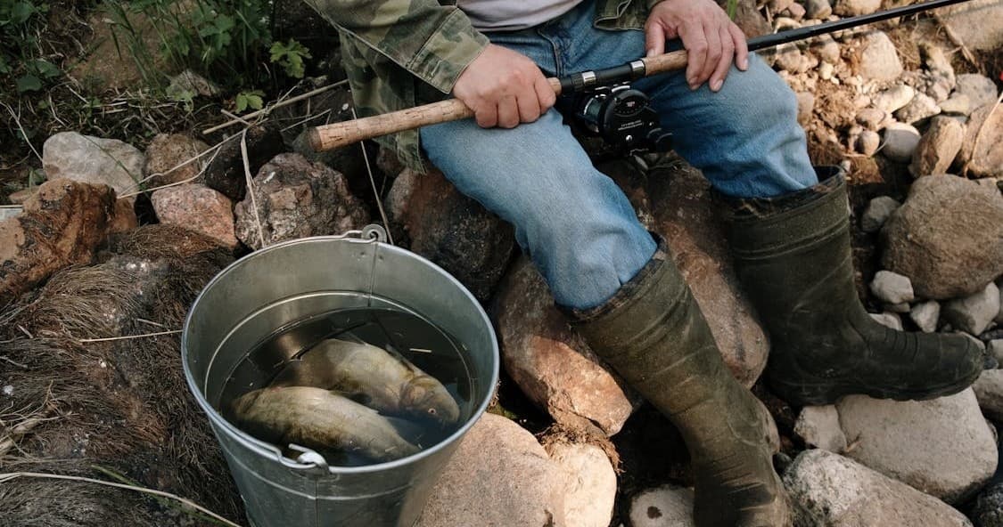 Angler with freshly caught fish in bucket on rocky shore