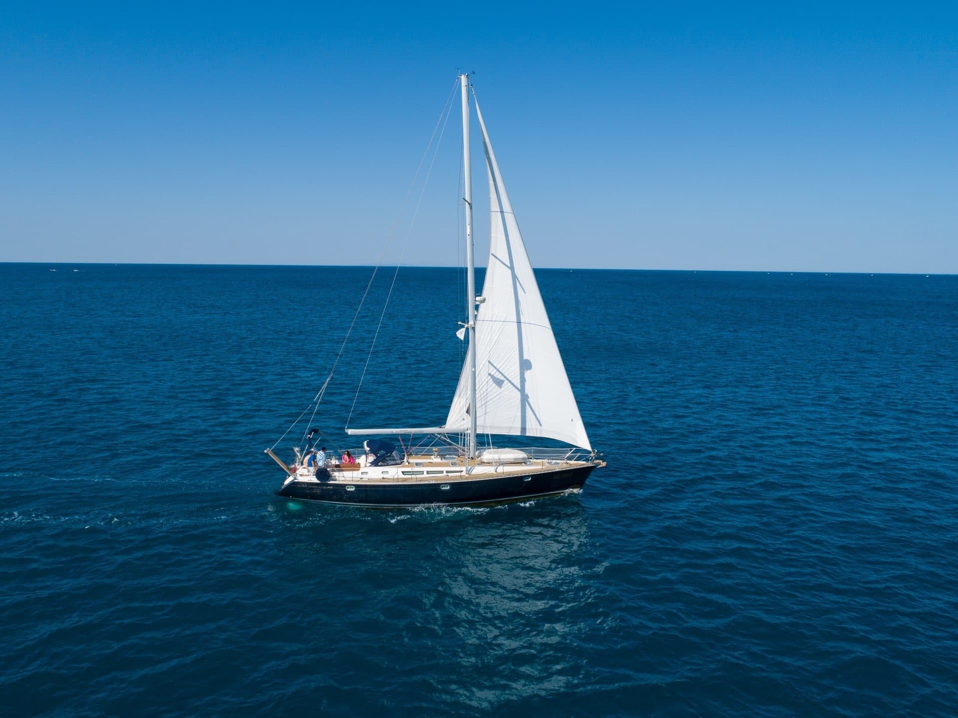 White-sailed yacht cruising open deep-blue ocean under clear sky