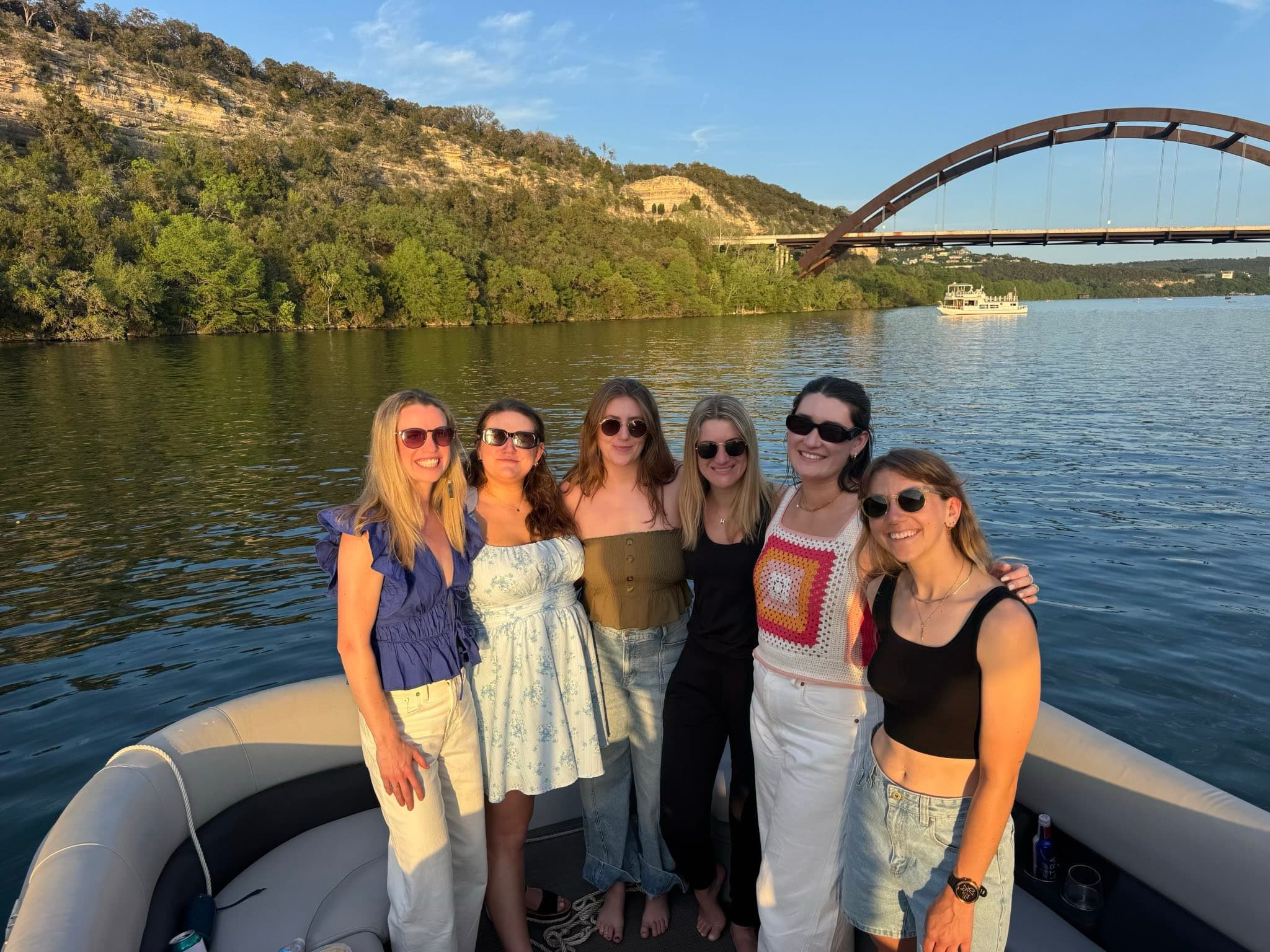 Friends posing on pontoon boat by scenic arched bridge on lake
